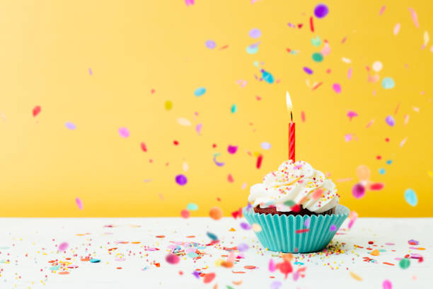 Birthday cupcake wih confetti on yellow background A colorful  birthday cupcake with one candle and confetti on a yellow background cupcake candle stock pictures, royalty-free photos & images