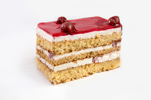 Slice of cherry glazed cake with fruit inside. Pastry dessert with cream and jam in layers.