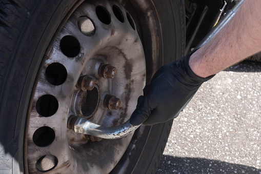male hands unscrew the bolts on the wheel from the car on the street