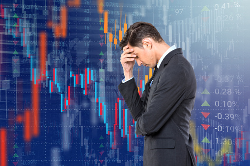 Worried businessman with head in hands in front of stock market data virtual interface