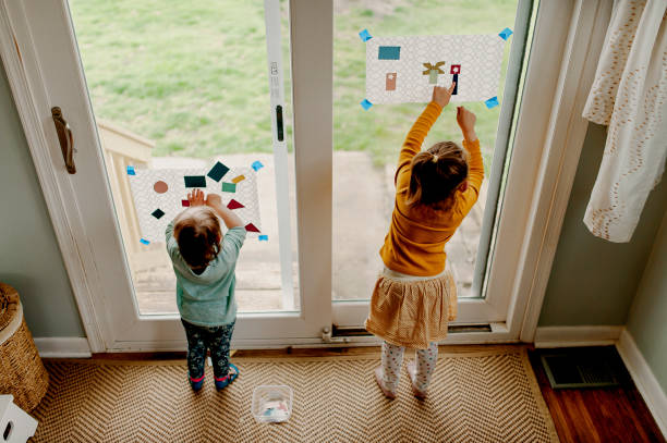 Rodzeństwo stojące przy suwaku, za pomocą papieru kontaktowego i próbek farby wyciętych w kształtach, aby tworzyć obrazy, aby zachować rozrywkę podczas kwarantanny – zdjęcie