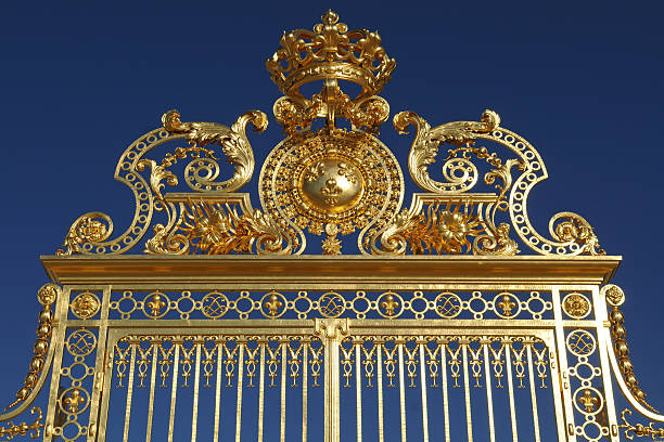 An ornated, majestic, golden gate against a clear blue sky.