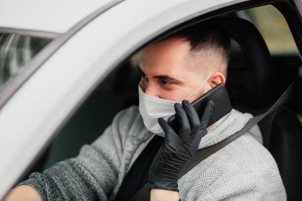 istock Man with protective mask and gloves driving a car talking on smartphone 1221882688