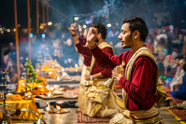 Men chanting at Ganga Aarti celebration on Dashashwamedh Ghat in Varanasi, India Varanasi, India - December 18, 2019: Ganga Aarti extravagant ritual ceremony, where some men pray and chant on some carpets with incense sticks, while a crowd of local people and tourists enjoy the celebration, in the night, in Varanasi, India. chanting stock pictures, royalty-free photos & images