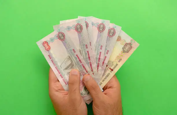 UAE national currency. UAE money banknotes. Young man holds in his hands dirhams on green background. AED.