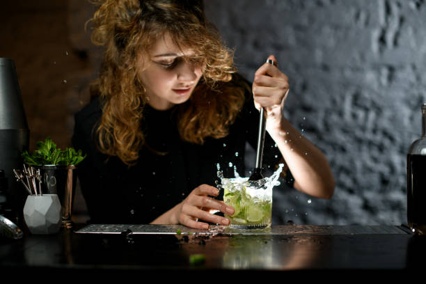 female bartender actively mixing cocktail using madler. female bartender actively mixing fresh caipirinha cocktail using madler. Splashes and drops of drink fly in different sides. pallet jack handle stock pictures, royalty-free photos & images