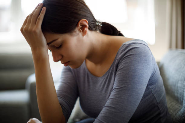 Upset woman sitting on sofa alone at home Upset woman sitting on sofa alone at home chronic illness stock pictures, royalty-free photos & images