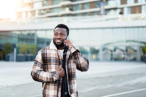 Happy young African American man talking on phone outdoors in the city.