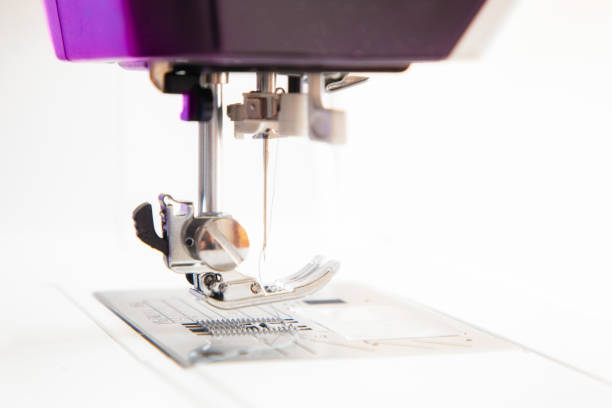 Sewing machine steel pressure foot with needle stitching with thread on blue fabric, textile on needle plate. Dressmaking, clothes industry, workshop and atelier company, business. Side view, closeup