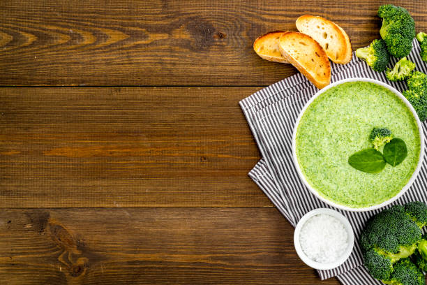 Broccoli cream soup on wooden kitchen table top view.