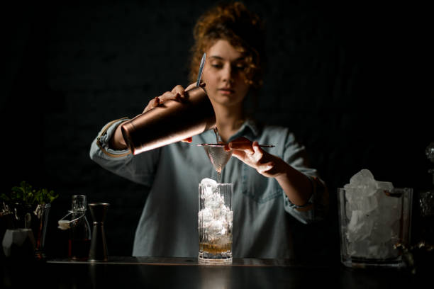 Professional female bartender pours finished cocktail to glass.