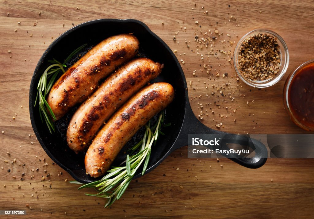 Sausages in a skillet Three sausages in a cast iron skillet with seasoning Sausage Stock Photo