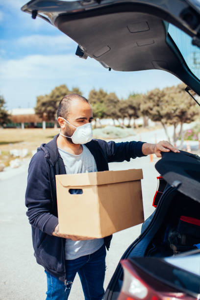 istock Man carrying box from his car, wearing protection mask 1221902812
