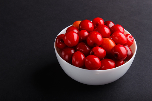 Fresh red sweet cherry in white bowl on black background. side view, close up.
