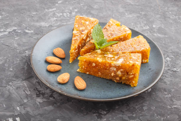 istock Traditional turkish candy cezerye made from caramelised melon, roasted walnuts, hazelnuts, pistachios in blue ceramic plate on a black concrete background. side view, flat lay, close up. 1221907544