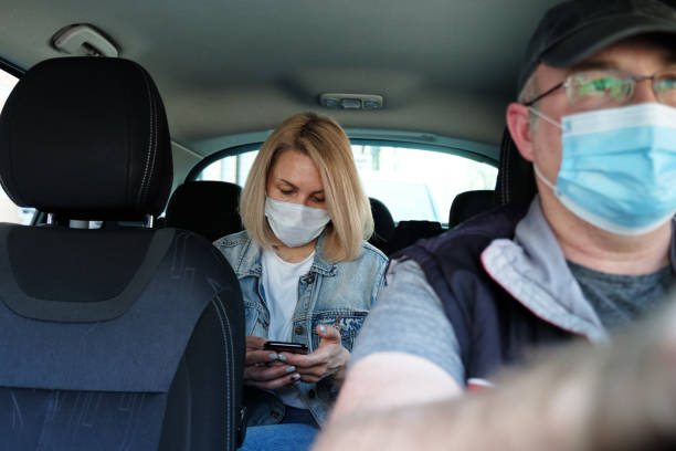 Taxi ride in time of Coronavirus Caucasian woman in taxi wearing face mask for protection from pollution and viruses such as Coronavirus. Using smartphone crowdsourced taxi stock pictures, royalty-free photos & images