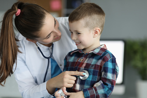 Close-up of smiling kid at doctors appointment. Professional pediatrician listening to heartbeat and checking child lugs. Planned checkup. Medicine and healthcare concept