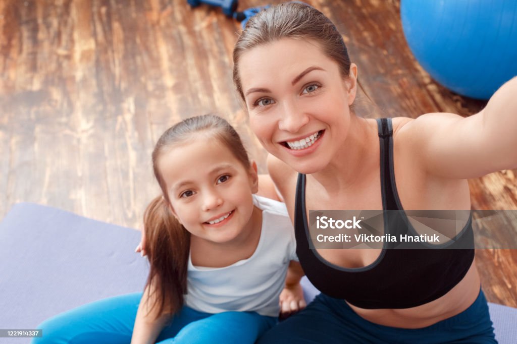 Estilo De Vida Saludable Madre E Hija En Ropa Deportiva Sentado En Estera De Yoga Tomando Selfie En El Teléfono Posando A La Cámara Sonriendo Alegre Primer Plano Foto de stock y Estilo De Vida Saludable Madre E Hija En Ropa Deportiva Sentado En Estera De Yoga Tomando Selfie En El Teléfono Posando A La Cámara Sonriendo Alegre Primer Plano Foto de stock y