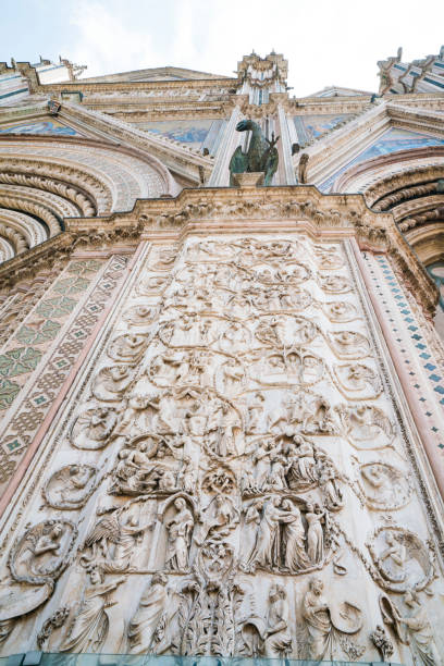 Low angle view of the bas-reliefs depicting episodes from the lives of Jesus and Mary in marble carvings with the bronze statue of the Easgle of John the Baptist on top of one of the 4 pillars on the facade of Orvieto's famous Duomo, Italy's boldest and most impressive Romanesque Gothic Cathedral, Orvieto, Italy, Europe