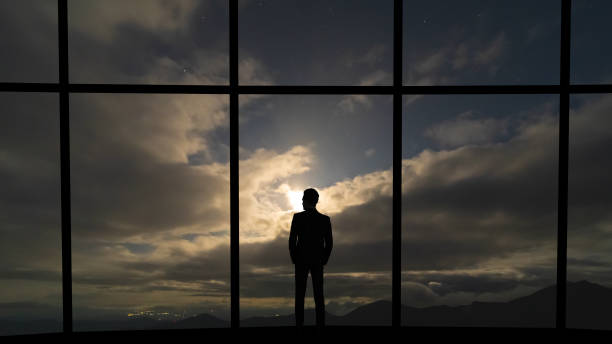 istock The businessman standing near the panoramic window on grey sky background 1221927978