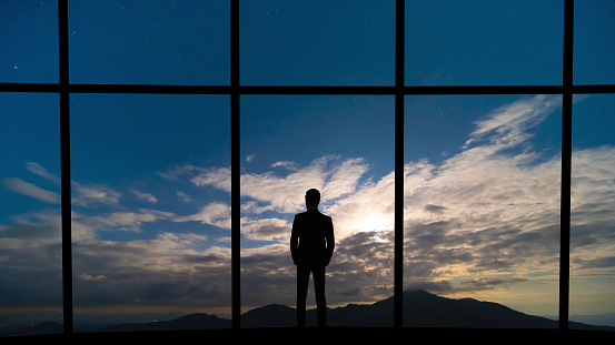 The businessman standing near the panoramic window on blue sky background