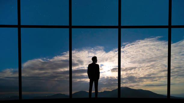 istock The businessman standing near the panoramic window on blue sky background 1221928000
