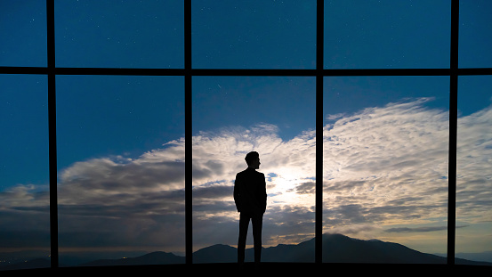 The businessman standing near the panoramic window on blue sky background