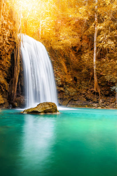 istock Waterfall and blue emerald water in autumn forest with sun flare 1221929843