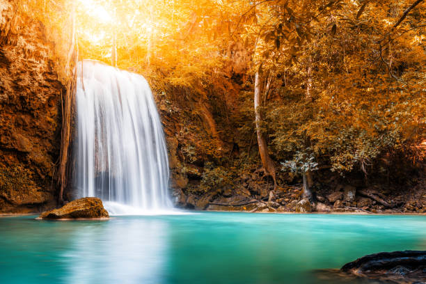 istock Waterfall and blue emerald water in autumn forest with sun flare 1221930954