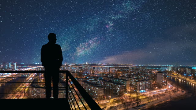 The man stands on the top of building on the starry cityscape background