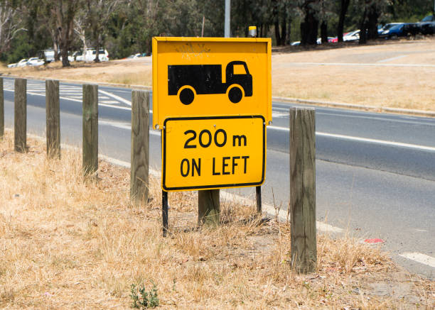 Photo of a black and yellow traffic warning sign beside a road