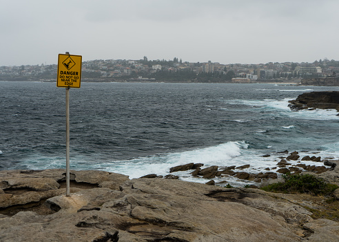 Photo of danger sign on rocky cliffs with sea and city in the background