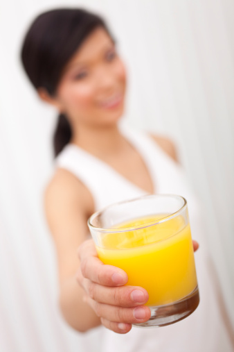 Selective focus photograph of beautiful Chinese Asian Asian girl or woman holding a glass of fresh pure orange juice to camera