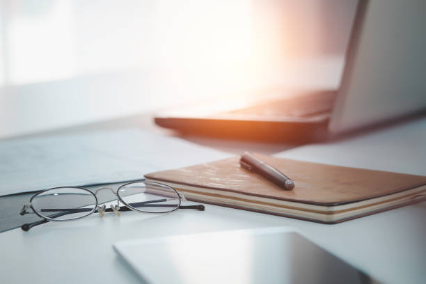 istock work from home, a glasses above laptop computer on a white modern business office desk table with a notebook and tablet with blank workspace for text input, interior design in calm concept 1221945472