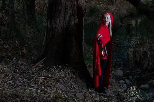 Attractive woman dressed a little red riding-hood walk in a dark forest with a lantern