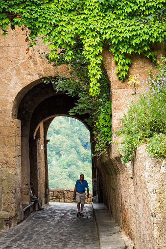 Civita di Bagnoregio, Viterbo, Itay - June 26, 2017: A senior male tourist enters the ancient Etuscan village of CivitÃ  di Bagnoregio, Civita Bagno, a hiulltop village perched atop volcanic tufta rock in southern Tuscany that is slowly eroding. Called the dying town because homes and a palace have collapsed and slid to the bottom of the valley in the eroding clay, Tuscany, Italy, Europe