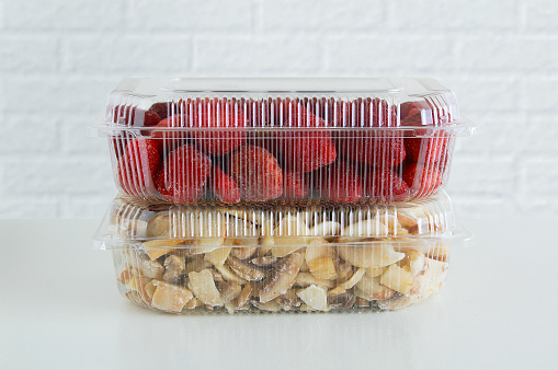 Frozen strawberries and champignons in a transparent plastic container on a white table.