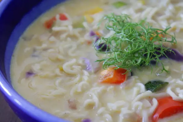 Photo showing a bowl of homemade spicy thai noodle soup / broth isolated on a blue background. This is a low calorie meal made with chopped vegetables and rice noodles, which are low in carbohydrate. This dish is part of a healthy eating, low fat diet plan.