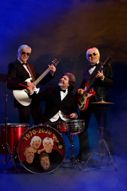 istock Musician group guitarist and drummer Active senior Handsome man playing guitar and drum. Best friends. Blue  background, with rays of light and special effects smoke. 1221962081