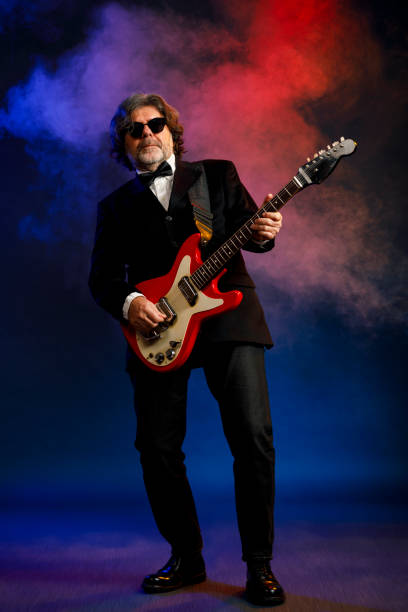 istock Musician Guitarist Active senior Handsome man playing guitar. Blue  background, with rays of light and special effects smoke. 1221962206