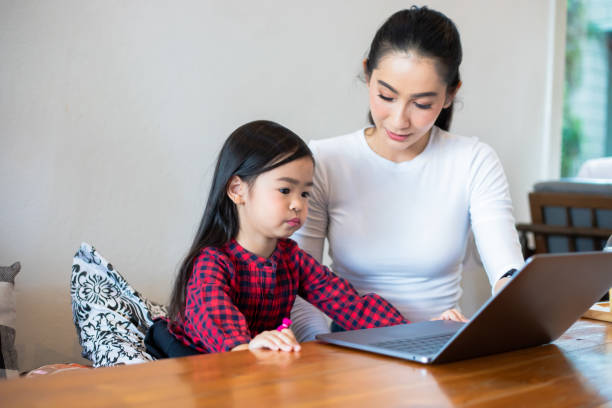 istock Asian mothers are teaching their daughters to read a book and use notebooks and technology for online learning during school holidays at home. Educational concepts and activities of the family 1221972253