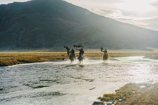 Eagle hunters riding through  the river in Mongolia