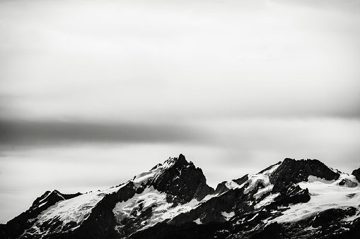 Long distance photograph of snowy mountain peaks with an overcast cloudy sky during winter
