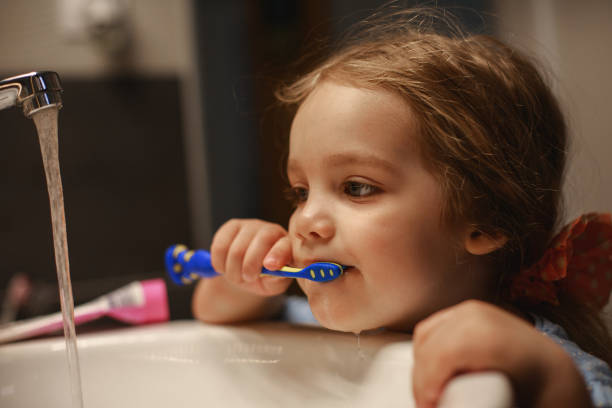 Little girl wasting water with tap open while brushing her teeth Front view of little girl using a tootbrush to clean her teeth before going to the bed during self-isolation. brushing teeth stock pictures, royalty-free photos & images