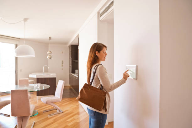 Woman activating smart home security system before leaving Woman activating smart home security system before leaving. The control panel is installed in the apartment on the wall. smart thermostat photos stock pictures, royalty-free photos & images