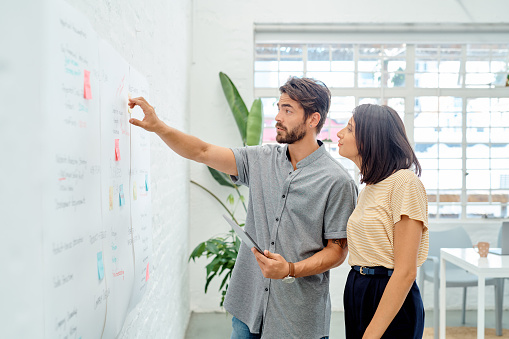 Shot of two businesspeople using a digital tablet while brainstorming with notes on a wall in an office