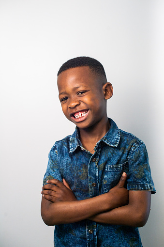 A cute African 6-7 year old boy portrait against a white background with arms crossed