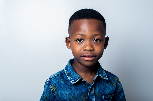 A cute African 6-7 year old boy portrait against a white background staring into camera.