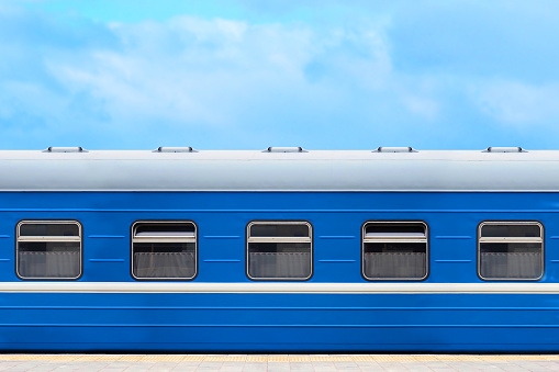 Blue passenger railway wagon on the platform, blue sky in the background