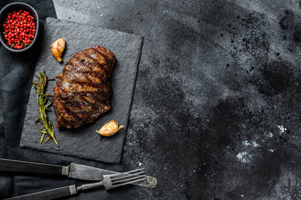 istock Grilled Flat Iron steak on a stone Board, marbled beef. Black background. Top view. Copy space 1221989676